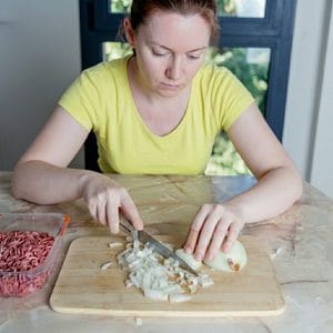 Cebolla picada en cuadritos disparejos en una tabla de cortar junto a un dedo con una curita, ilustrando los riesgos comunes al aprender cómo picar cebolla en cuadritos.