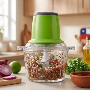 Picadora eléctrica de verduras picando pebre chileno con ingredientes frescos a su alrededor.