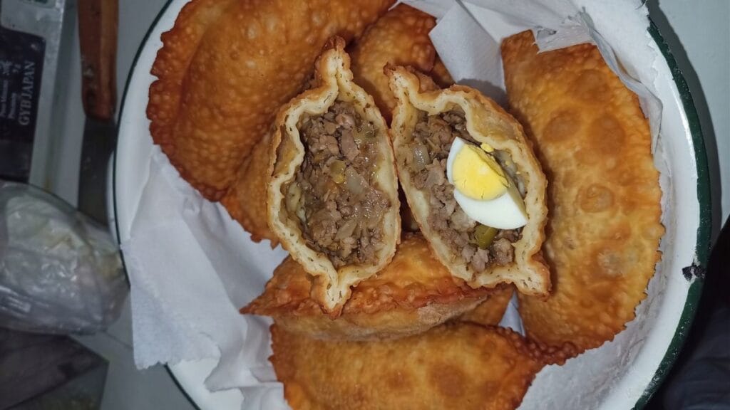 Empanadas fritas doradas y crujientes servidas en una fuente enlozada, mostrando el relleno de pino chileno tradicional con carne, cebolla y un trozo de huevo duro.
